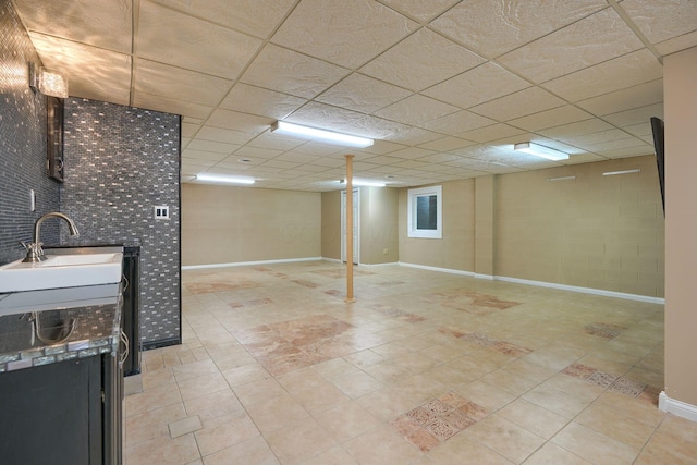 basement featuring a paneled ceiling, light tile patterned floors, and sink