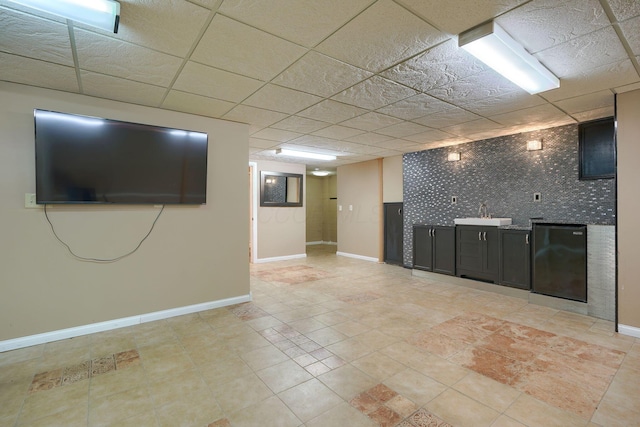 basement with a paneled ceiling, refrigerator, and sink