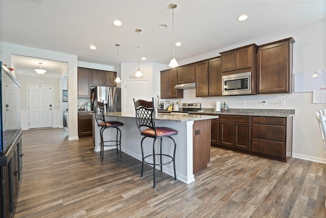 kitchen with decorative light fixtures, light stone countertops, an island with sink, a kitchen breakfast bar, and stainless steel appliances