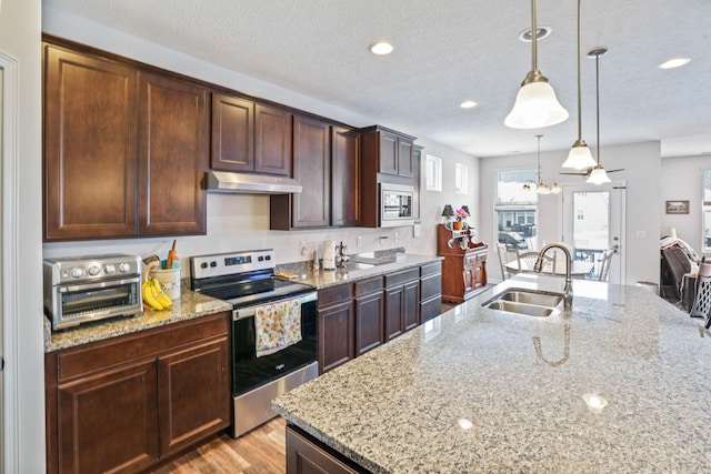 kitchen with light stone counters, sink, hanging light fixtures, and stainless steel appliances