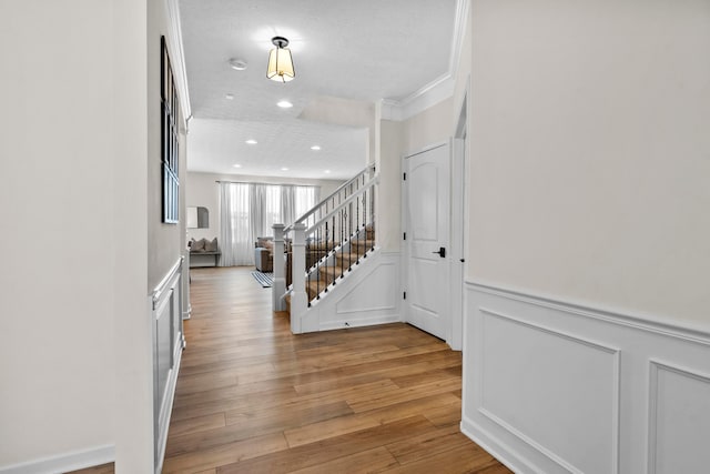 foyer featuring a textured ceiling, light wood-type flooring, and crown molding