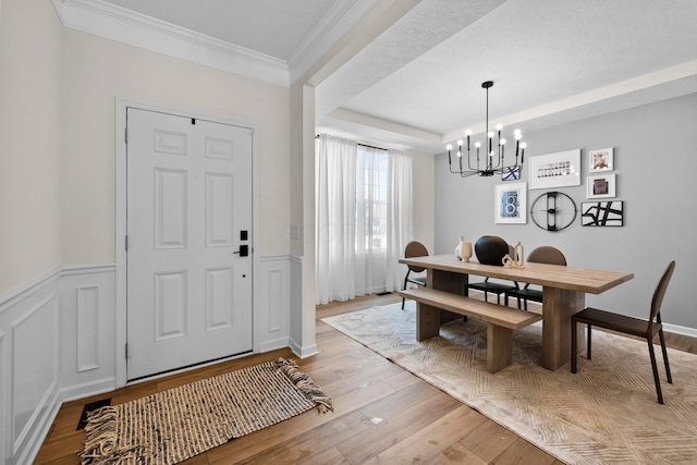 dining space featuring a notable chandelier, crown molding, a tray ceiling, and light hardwood / wood-style flooring