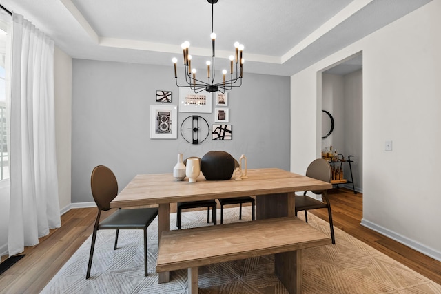 dining area with a notable chandelier, a tray ceiling, and light hardwood / wood-style flooring