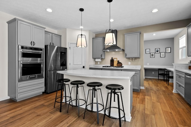 kitchen featuring appliances with stainless steel finishes, gray cabinetry, wall chimney range hood, pendant lighting, and a kitchen island