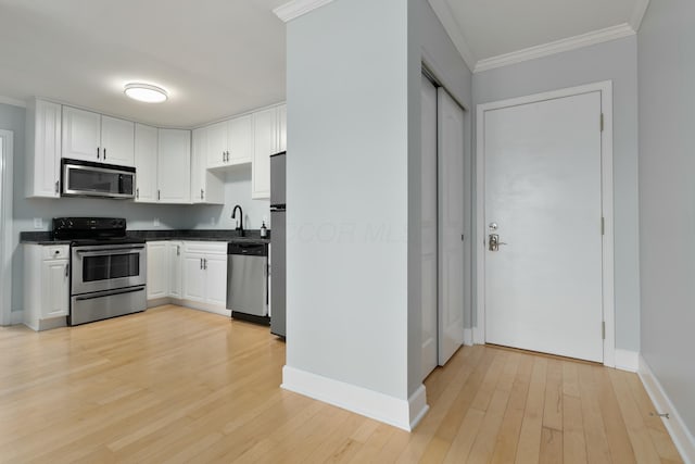 kitchen with light wood-type flooring, white cabinetry, stainless steel appliances, and ornamental molding