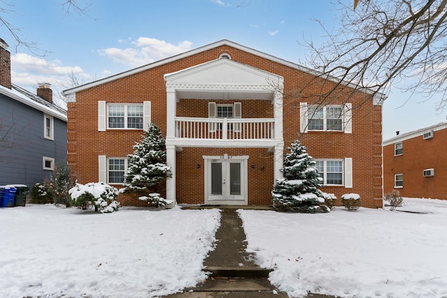 snow covered back of property featuring a balcony and french doors