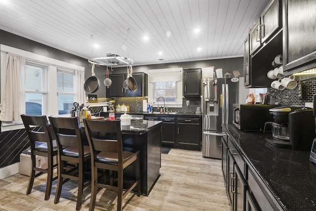 kitchen featuring sink, dark stone countertops, stainless steel fridge with ice dispenser, light hardwood / wood-style floors, and a breakfast bar area