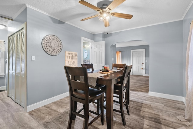 dining area with a textured ceiling, light wood-type flooring, ceiling fan, and crown molding