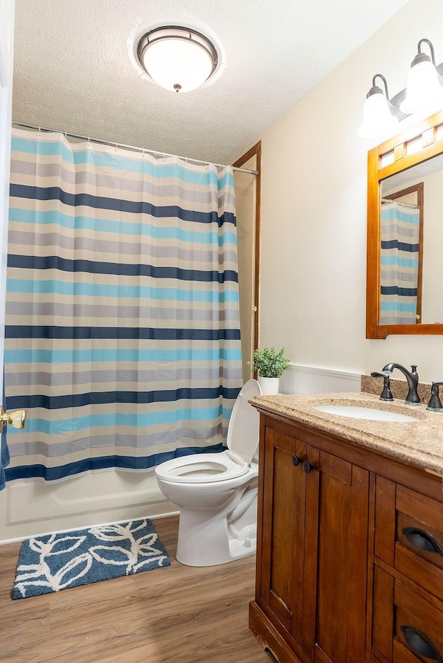 full bathroom with vanity, a textured ceiling, shower / bath combo with shower curtain, wood-type flooring, and toilet