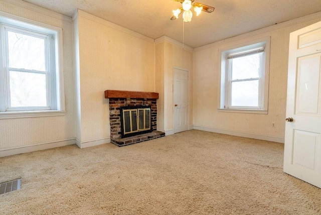 unfurnished living room featuring ceiling fan, crown molding, carpet floors, and a brick fireplace