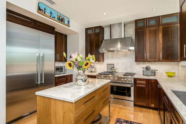 kitchen with light stone countertops, wall chimney range hood, tasteful backsplash, a kitchen island, and high end appliances