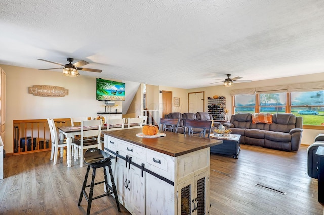 kitchen with wood counters, a textured ceiling, ceiling fan, wood-type flooring, and a center island