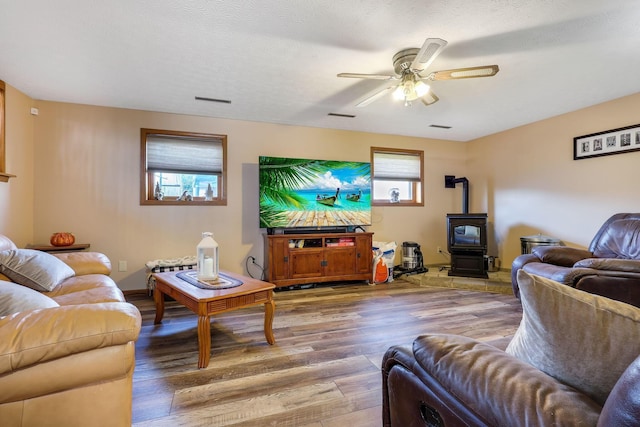 living room featuring a wood stove, ceiling fan, wood-type flooring, and a textured ceiling