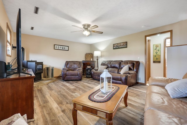 living room with light wood-type flooring, a textured ceiling, ceiling fan, a wood stove, and plenty of natural light