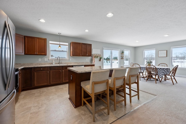 kitchen featuring sink, light stone counters, decorative light fixtures, stainless steel refrigerator, and a kitchen island