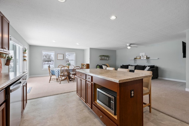 kitchen with a breakfast bar area, a center island, stainless steel appliances, light carpet, and a textured ceiling