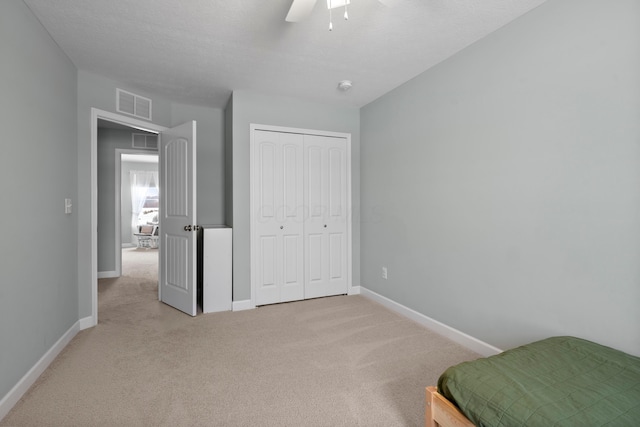 bedroom with light colored carpet, a textured ceiling, ceiling fan, and a closet