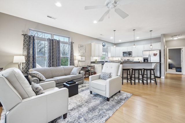 living room with light wood-type flooring, ceiling fan, and sink