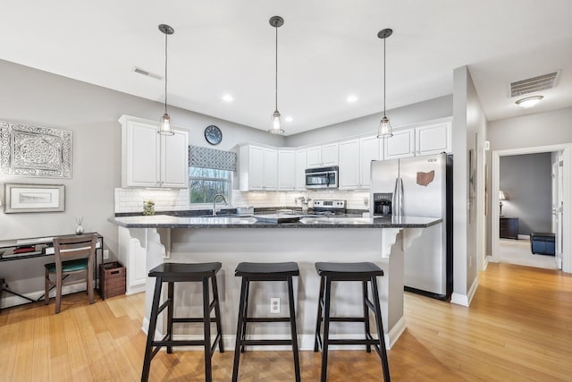 kitchen featuring a breakfast bar area, stainless steel appliances, dark stone counters, decorative backsplash, and white cabinetry