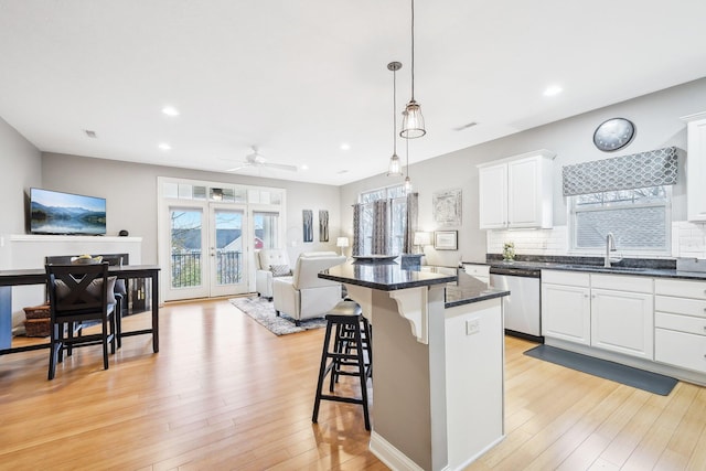 kitchen with sink, white cabinetry, a kitchen bar, stainless steel dishwasher, and hanging light fixtures