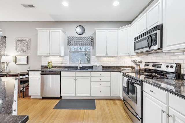 kitchen featuring stainless steel appliances, light hardwood / wood-style floors, white cabinets, dark stone counters, and sink