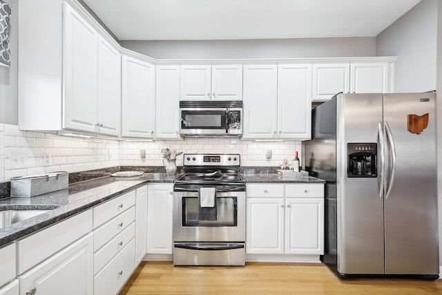 kitchen with light hardwood / wood-style flooring, decorative backsplash, white cabinets, dark stone counters, and appliances with stainless steel finishes