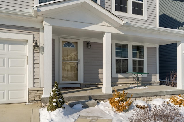 snow covered property entrance featuring a porch and a garage