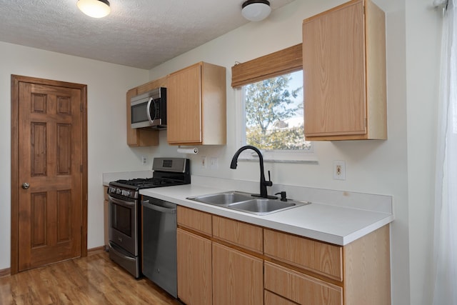 kitchen with light wood-type flooring, sink, a textured ceiling, appliances with stainless steel finishes, and light brown cabinetry