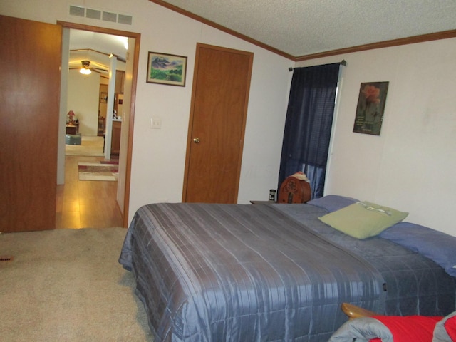 carpeted bedroom with lofted ceiling, a textured ceiling, visible vents, ensuite bath, and crown molding