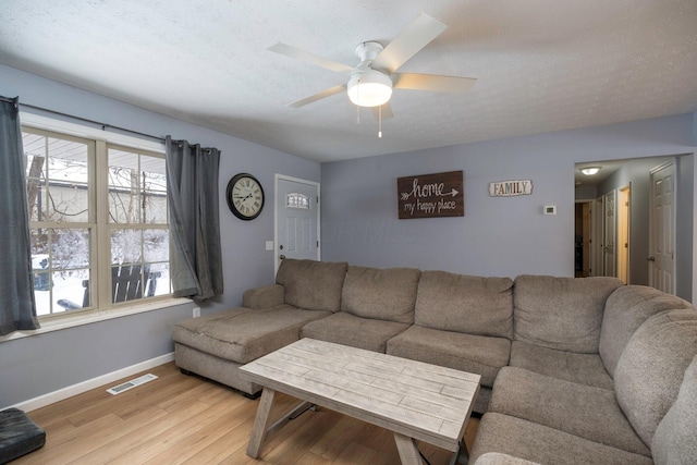 living area featuring visible vents, light wood-style flooring, a textured ceiling, baseboards, and ceiling fan