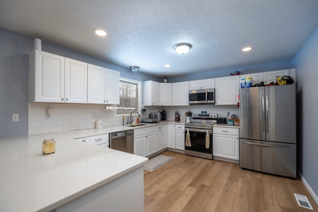 kitchen featuring visible vents, light wood-type flooring, appliances with stainless steel finishes, white cabinets, and a sink