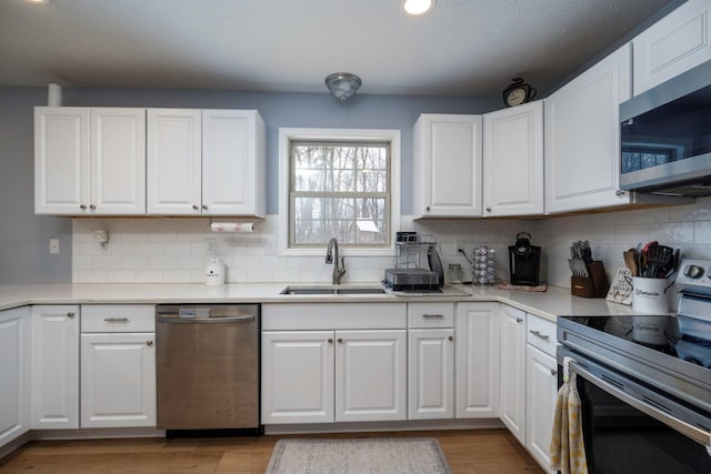 kitchen with light wood finished floors, a sink, white cabinets, appliances with stainless steel finishes, and backsplash