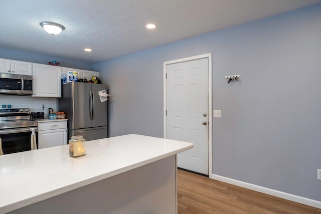 kitchen with baseboards, decorative backsplash, white cabinets, light wood-style floors, and appliances with stainless steel finishes