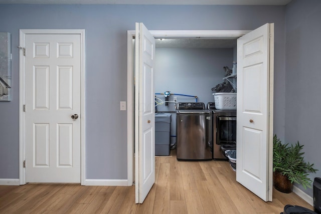 laundry room with light wood-type flooring, baseboards, washing machine and dryer, and laundry area