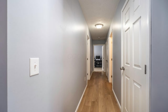 hall with baseboards, light wood finished floors, and a textured ceiling