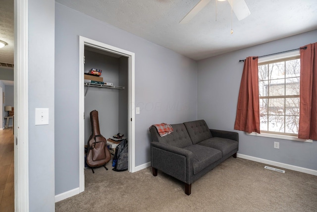 living area with visible vents, baseboards, ceiling fan, light colored carpet, and a textured ceiling