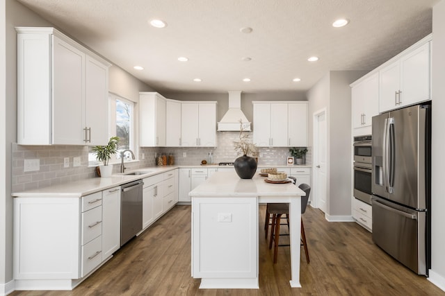 kitchen with premium range hood, stainless steel appliances, sink, white cabinets, and a kitchen island