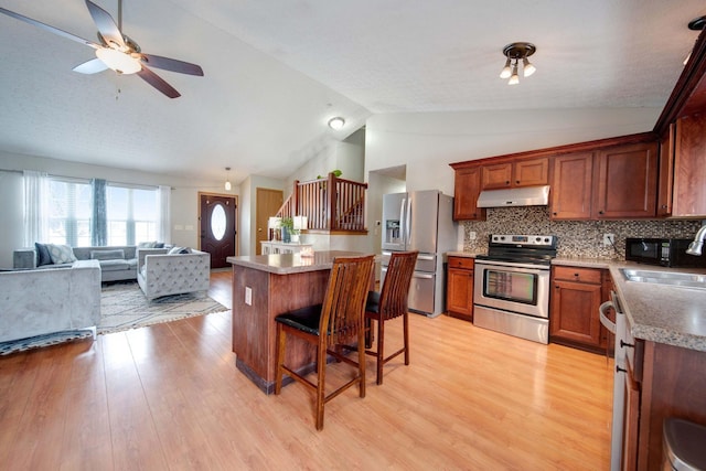 kitchen with sink, vaulted ceiling, decorative backsplash, appliances with stainless steel finishes, and light wood-type flooring