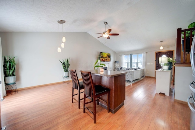 kitchen featuring a breakfast bar, ceiling fan, decorative light fixtures, light hardwood / wood-style flooring, and lofted ceiling