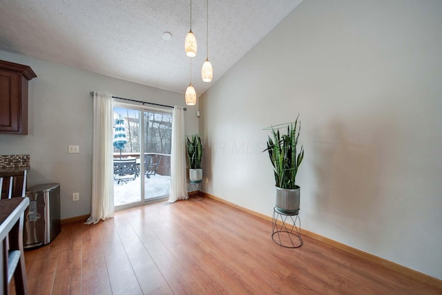 dining area featuring a textured ceiling, light hardwood / wood-style floors, and lofted ceiling