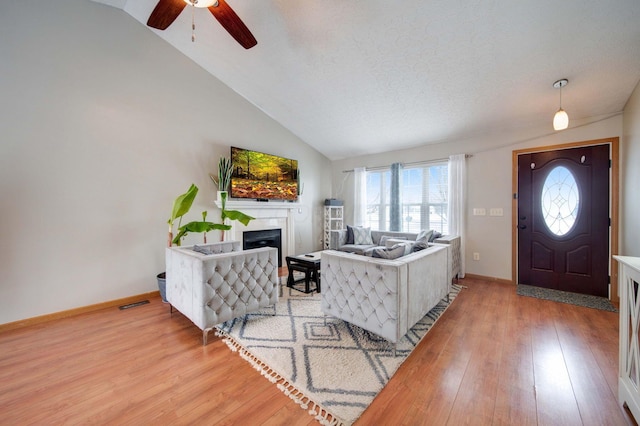 living room featuring a textured ceiling, ceiling fan, vaulted ceiling, and light wood-type flooring