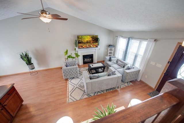 living room featuring vaulted ceiling, ceiling fan, light hardwood / wood-style floors, and a textured ceiling