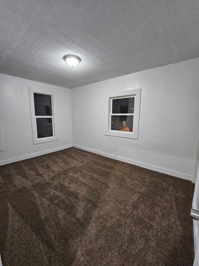 empty room with dark colored carpet and a textured ceiling