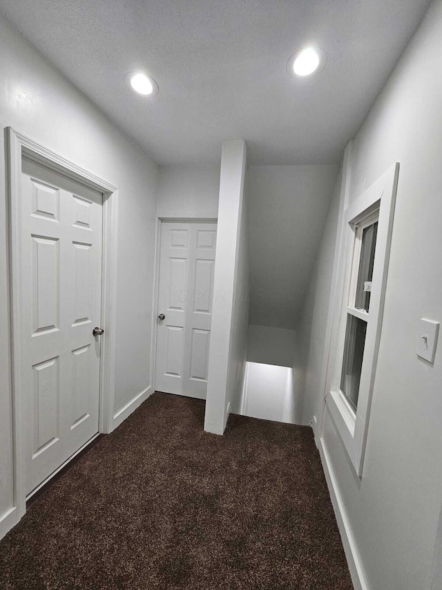 hall featuring dark colored carpet and a textured ceiling