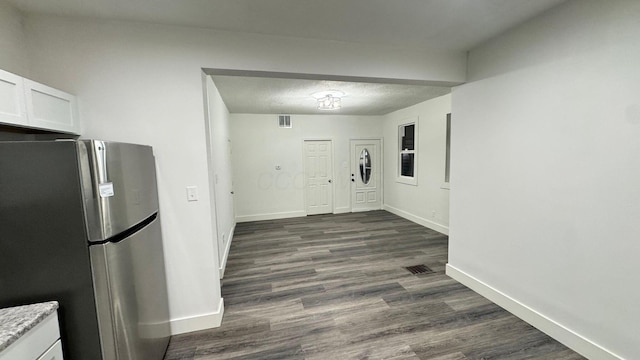 kitchen featuring white cabinets, dark hardwood / wood-style flooring, light stone countertops, and stainless steel refrigerator