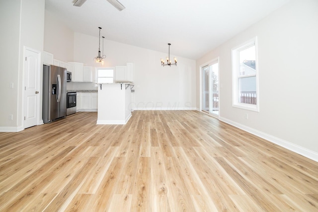 unfurnished living room featuring ceiling fan with notable chandelier, high vaulted ceiling, and light hardwood / wood-style flooring