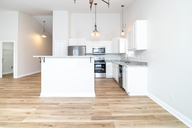 kitchen featuring white cabinets, sink, a towering ceiling, appliances with stainless steel finishes, and a kitchen island