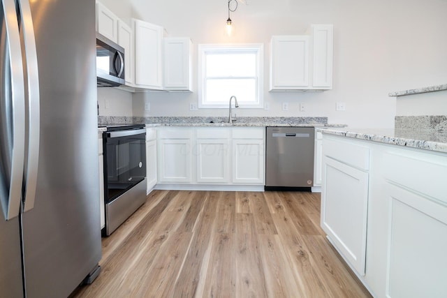 kitchen featuring white cabinets, light wood-type flooring, stainless steel appliances, and light stone counters