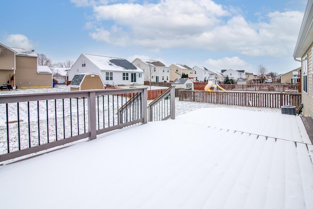 snow covered deck featuring a playground, central AC unit, and a storage shed