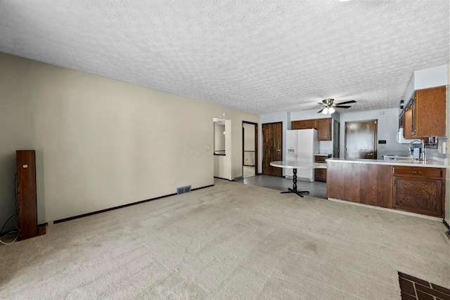 unfurnished living room featuring ceiling fan, light colored carpet, sink, and a textured ceiling